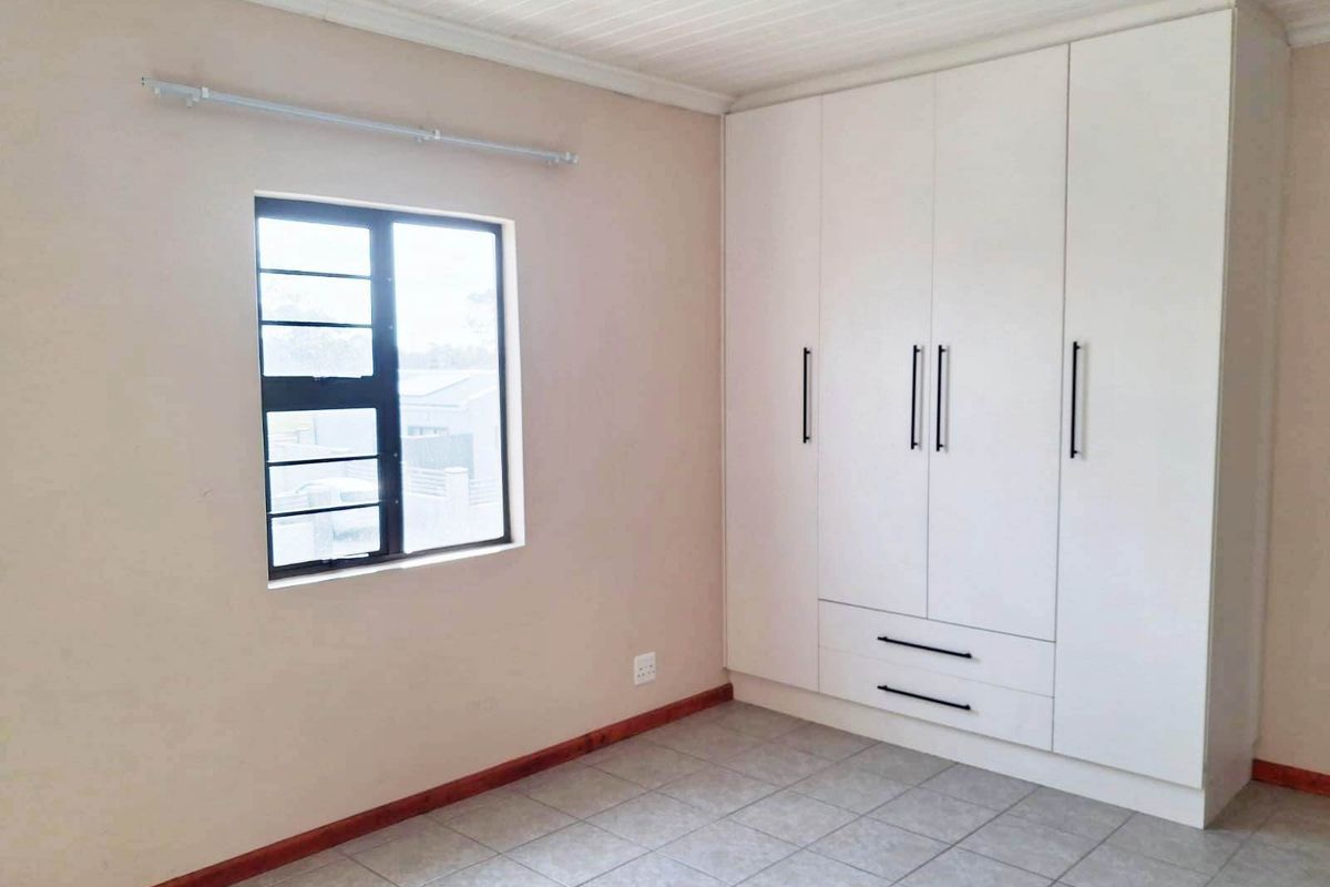 A clean, empty bedroom featuring neutral walls, tiled flooring, a tongue and groove ceiling, and a large white built-in wardrobe.