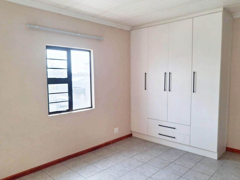 A clean, empty bedroom featuring neutral walls, tiled flooring, a tongue and groove ceiling, and a large white built-in wardrobe.