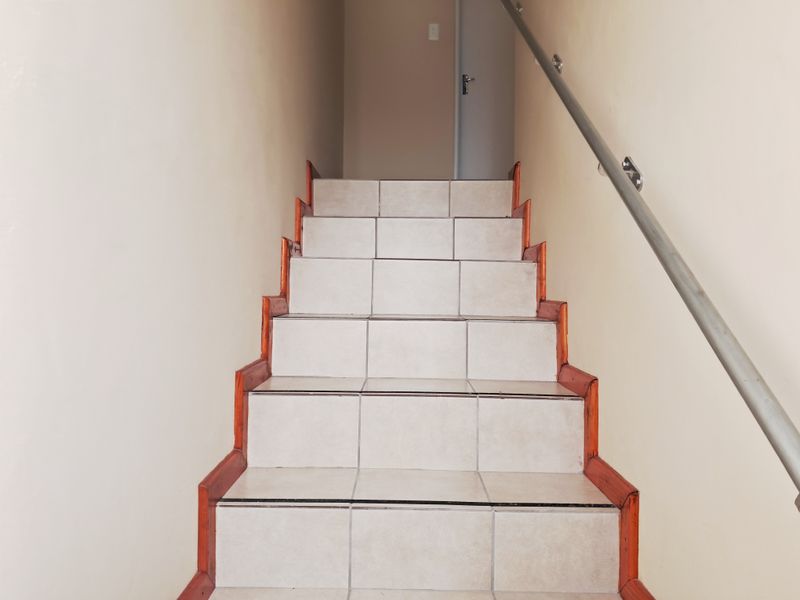 A staircase featuring tiled steps with wooden trim and a metal handrail, leading to an upper landing.