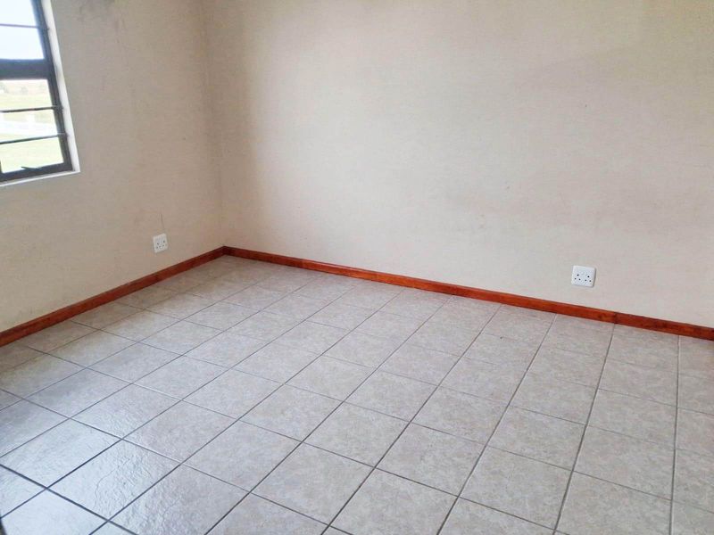 An empty bedroom featuring neutral tiled flooring, timber skirting boards, and a single window, providing a blank canvas for interior design.