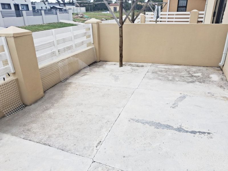 A paved outdoor patio area enclosed by boundary walls, featuring a central post and perimeter fencing.