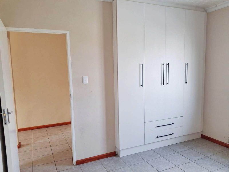 A clean, empty bedroom featuring modern white built-in cupboards and neutral tiled flooring, providing a versatile space ready for personalization.