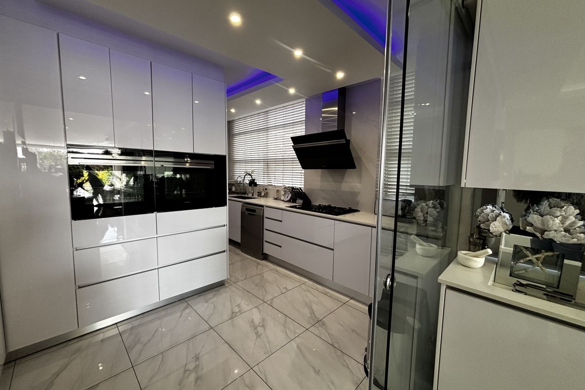 Modern kitchen featuring high-gloss white cabinetry, integrated appliances, marble-look floor tiles, and recessed ceiling lighting with ambient LED accents.