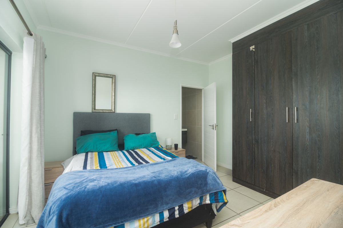 A bedroom featuring built-in dark wood-grain wardrobes, tiled flooring, and an en-suite bathroom entrance.