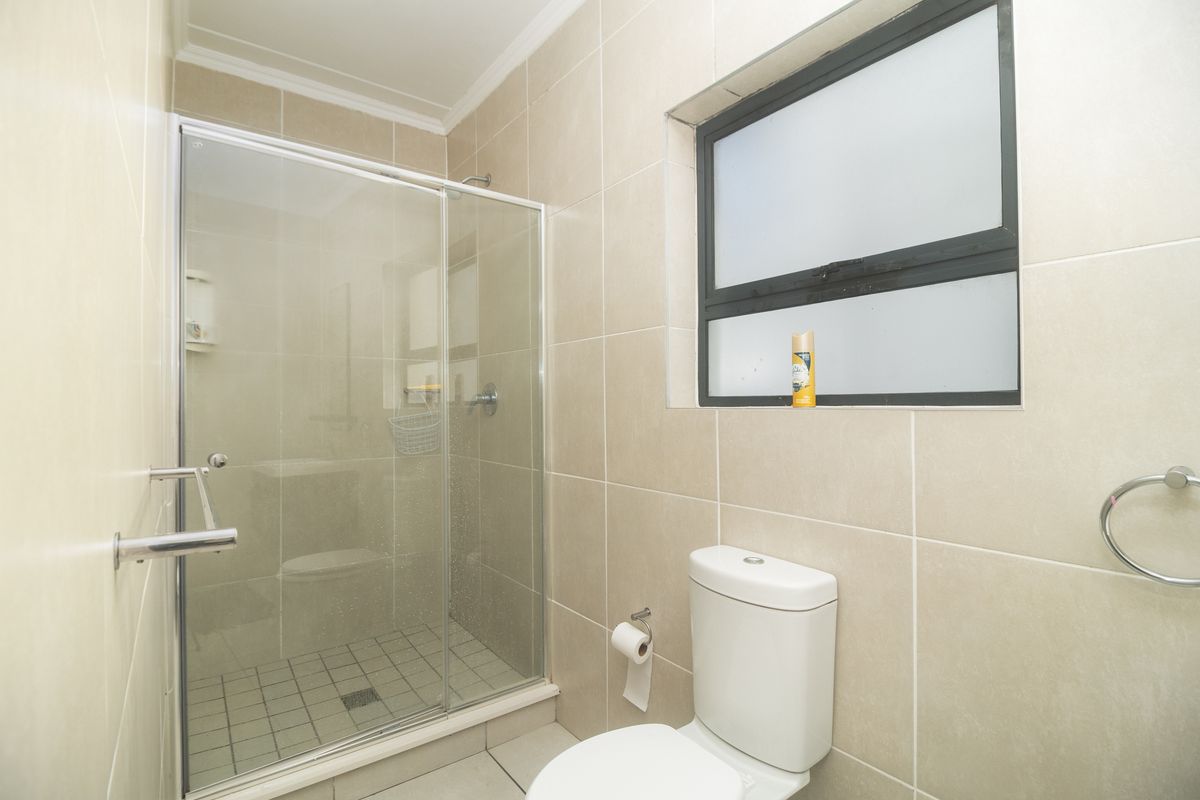 A functional bathroom featuring a glass-enclosed shower, tiled walls, and a standard toilet with a frosted window for privacy.