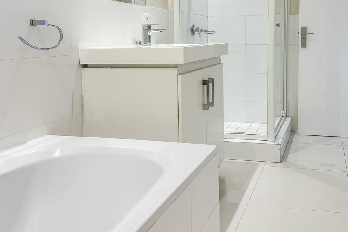 A clean, modern bathroom featuring a white vanity, a separate glass-enclosed shower, and a built-in bathtub with white tiled flooring.