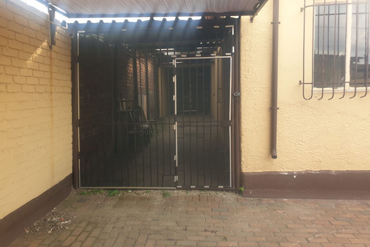 A secure side passage or utility area featuring a metal security gate, brick paving, and protective security bars on the window.