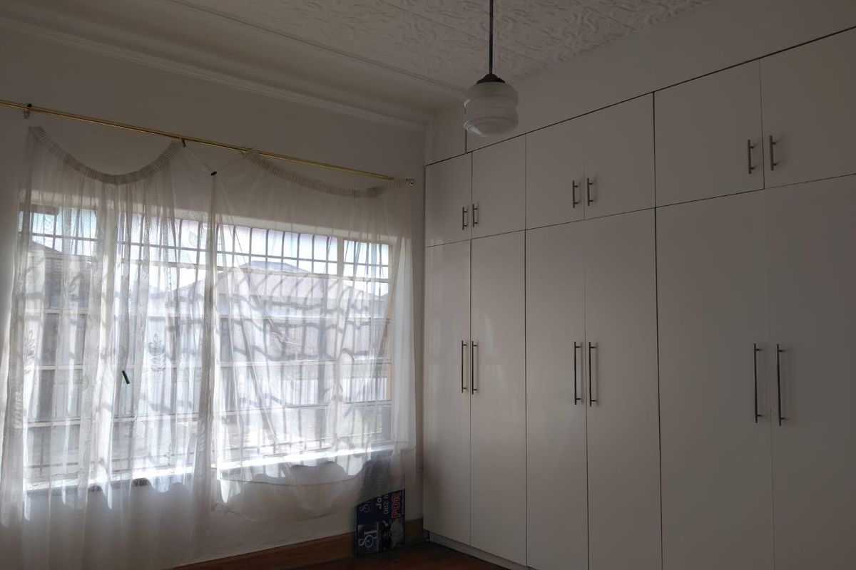 A bright bedroom featuring polished wooden flooring, a decorative pressed ceiling, and extensive floor-to-ceiling built-in cabinetry.