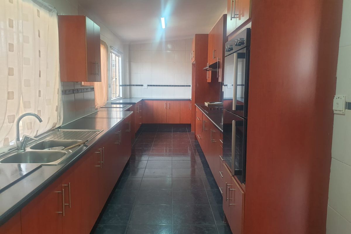 A functional galley-style kitchen featuring dark tiled flooring, ample wooden cabinetry, integrated double oven, and a stainless steel double sink.