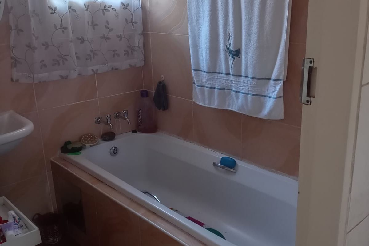 A functional bathroom featuring a built-in bathtub with wall-mounted taps and full-height wall tiling.