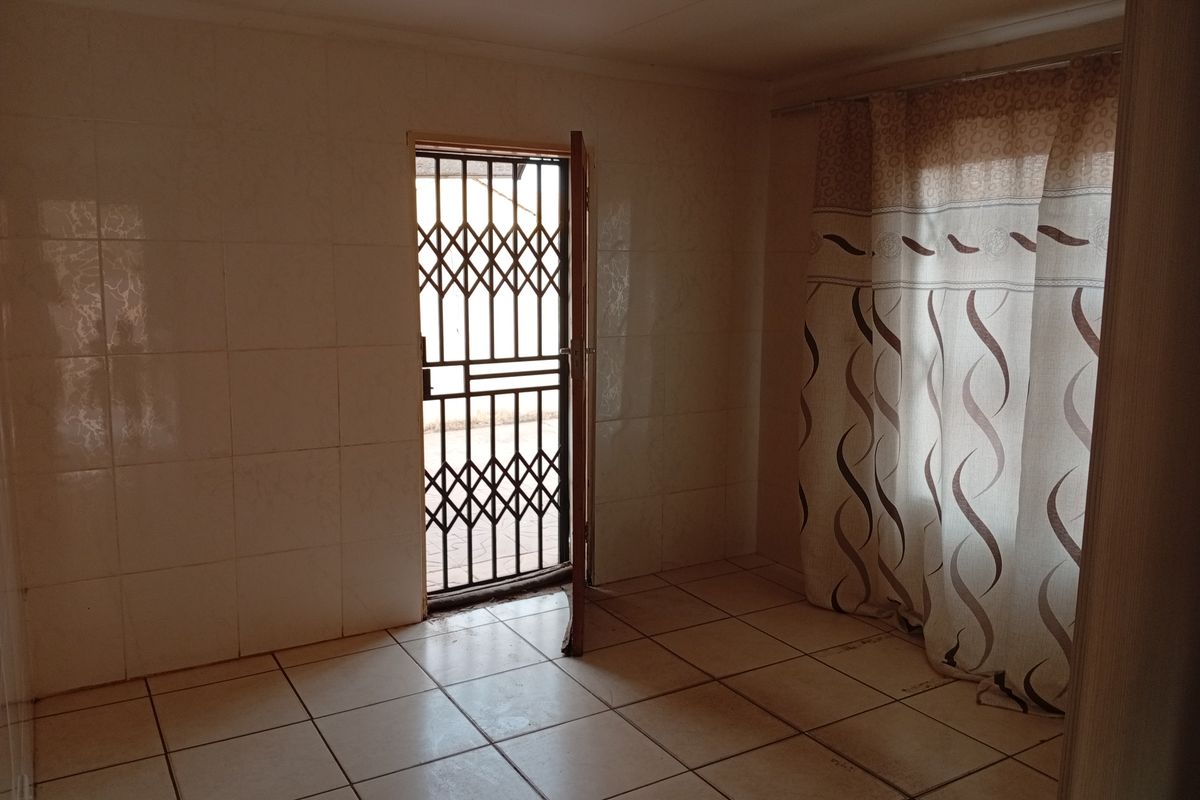 An empty room featuring tiled walls and flooring, with a security gate at the entrance and a window covered by curtains.