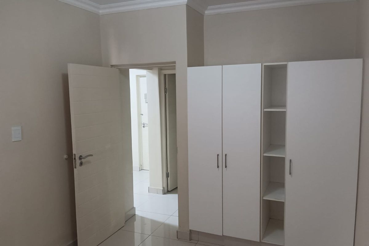 A bedroom interior featuring built-in white cabinetry, tiled flooring, and crown molding, with an open doorway leading to a hallway.