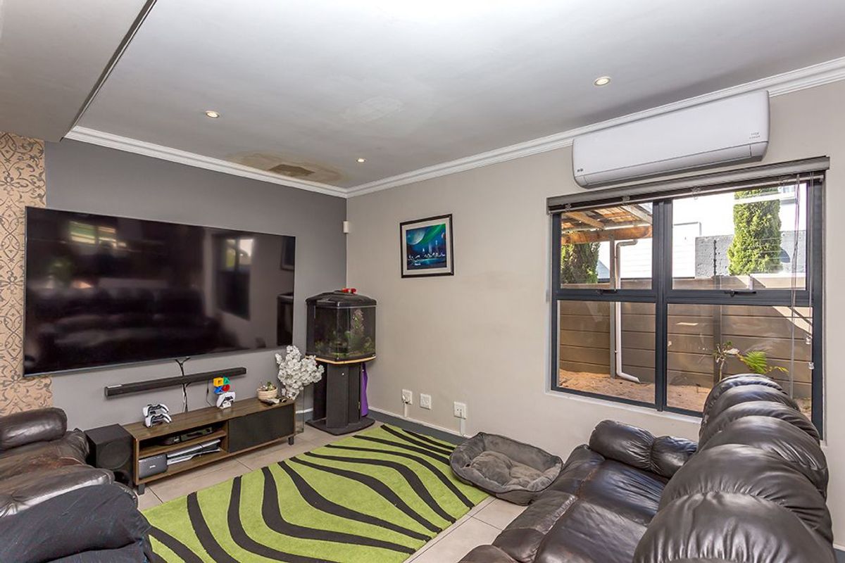 A comfortable living room featuring tiled flooring, a wall-mounted air conditioning unit, and large windows providing natural light.
