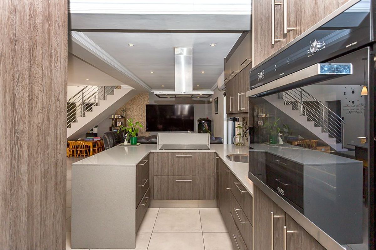 Modern kitchen featuring sleek wood-grain cabinetry, stone countertops, a central island with a built-in cooktop, and a stainless steel extractor fan.