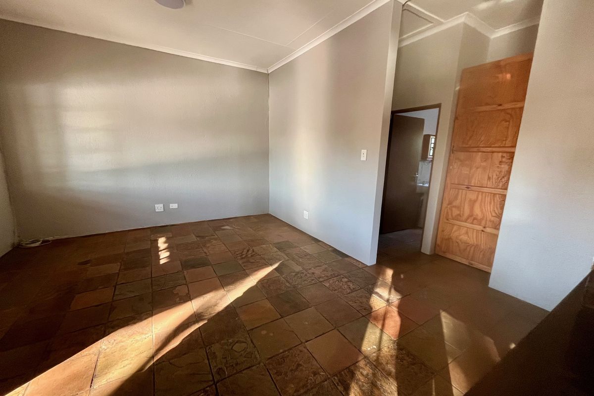 An empty living area featuring rustic terracotta-style floor tiles, neutral wall paint, and a wooden door leading to an adjacent room.