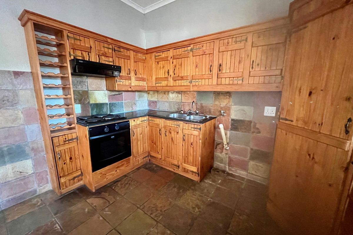 A dated kitchen featuring rustic wooden cabinetry, a stone tile backsplash, built-in oven and hob, and stone floor tiles.