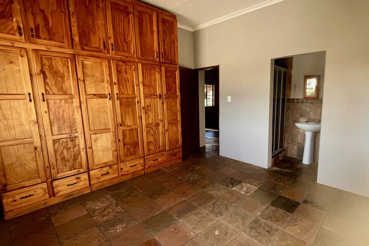 Bedroom featuring extensive built-in wooden cabinetry, stone tile flooring, and an en-suite bathroom with a pedestal basin and shower.