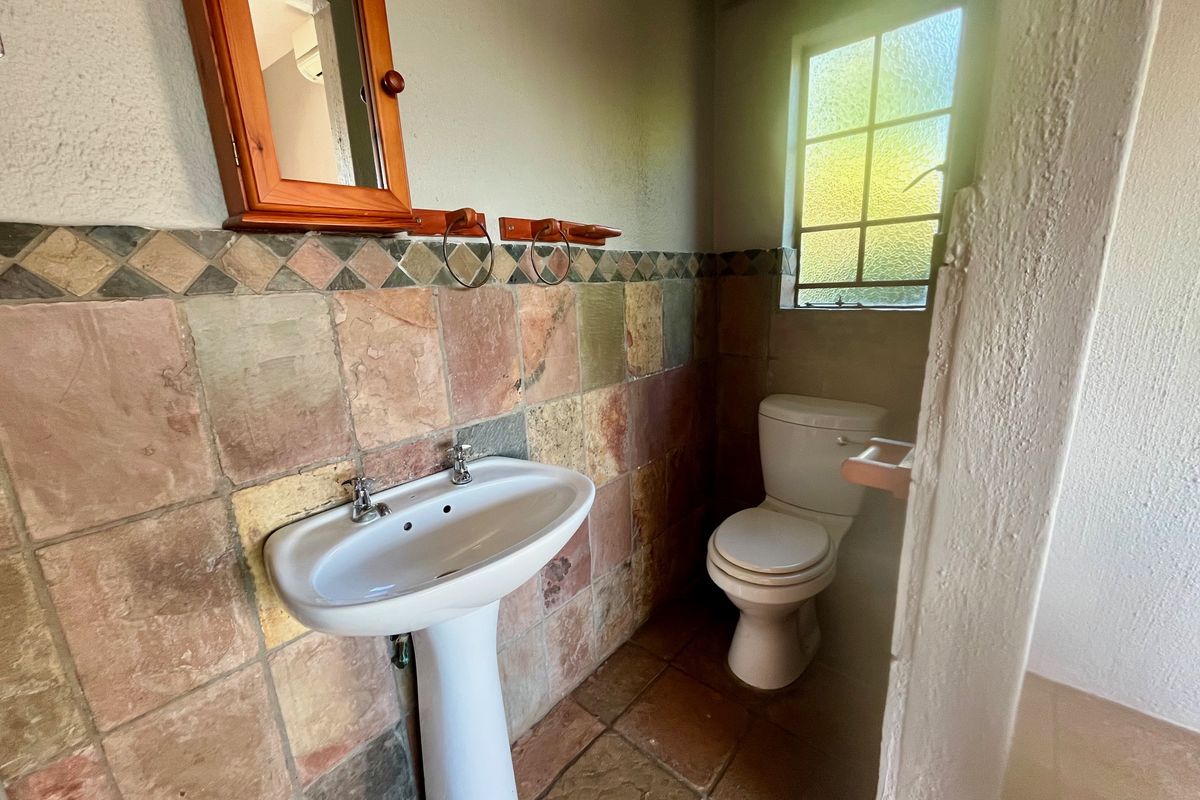 A functional bathroom featuring a pedestal basin, a standard toilet, and rustic stone-style wall and floor tiling.