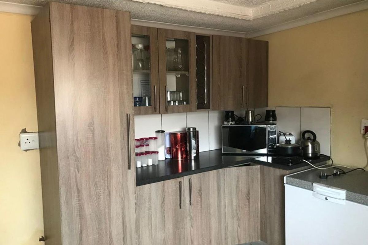 A compact kitchen area featuring wood-look cabinetry, dark laminate countertops, and tiled splashbacks, requiring some finishing touches to the surrounding walls and electrical points.