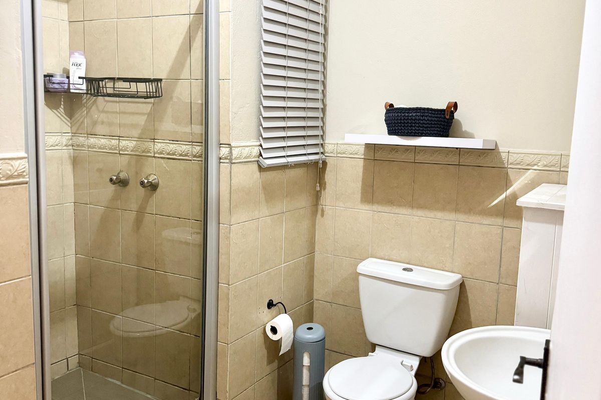 A functional bathroom featuring a glass-enclosed shower, pedestal sink, and toilet, finished with neutral ceramic wall and floor tiles.