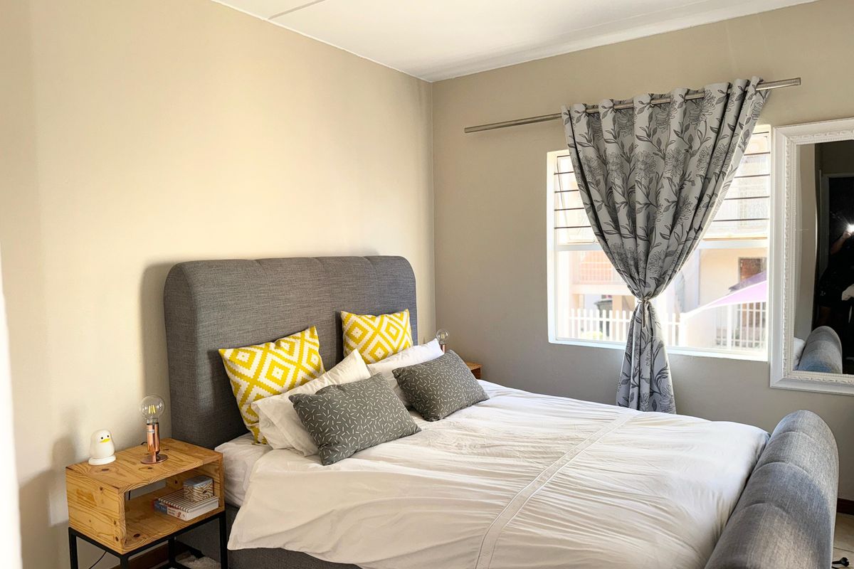 A well-maintained bedroom featuring neutral wall tones, a large window with curtain rod, and clean flooring.