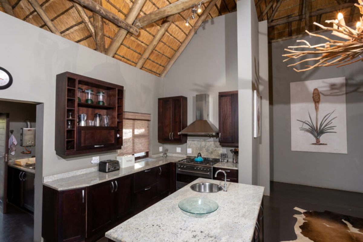 A kitchen featuring dark wood cabinetry, granite countertops, a central island with a prep sink, and a high vaulted thatched ceiling.