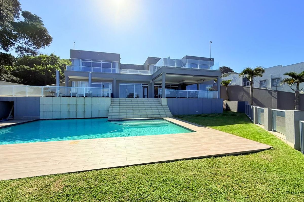 A modern rear exterior view featuring a swimming pool, tiled pool deck, landscaped lawn, and a multi-level terrace with glass balustrades.