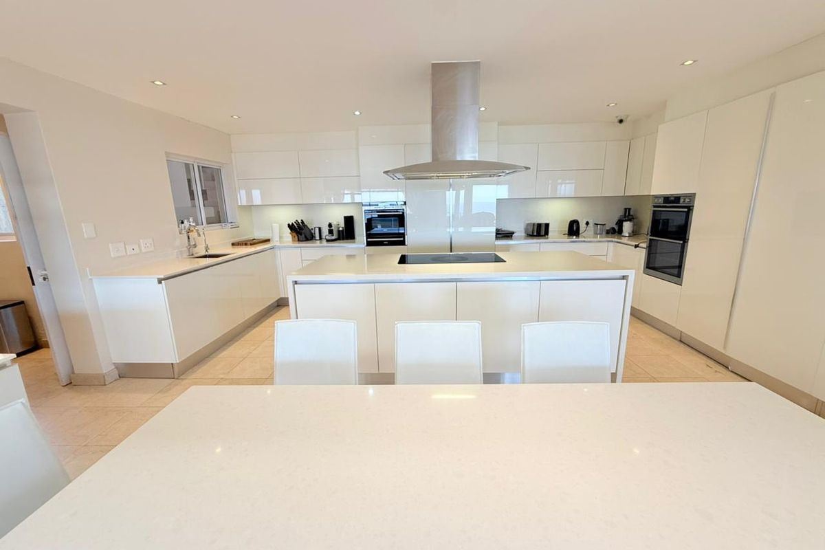 Modern kitchen featuring high-gloss cabinetry, a central island with integrated hob, stainless steel extractor fan, and built-in double ovens.