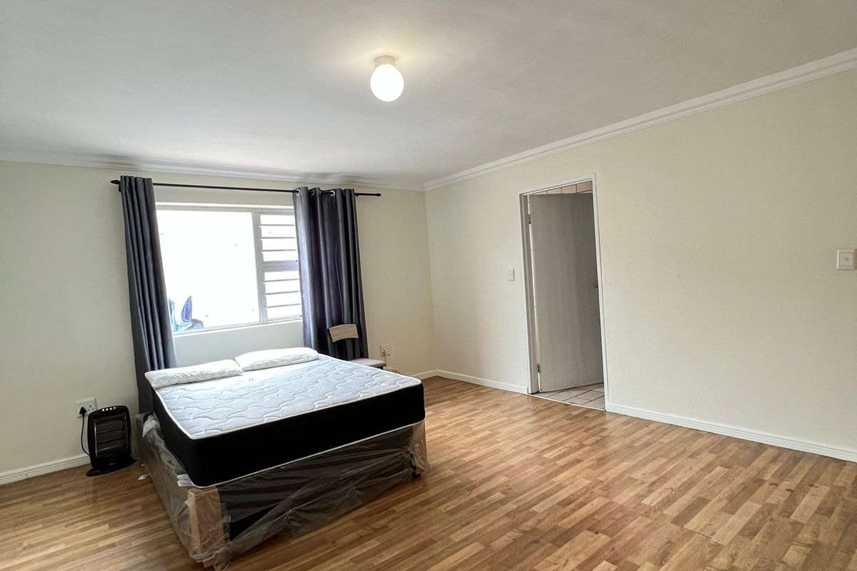Spacious bedroom featuring wood-look laminate flooring, neutral walls, and a large window with curtain rails.