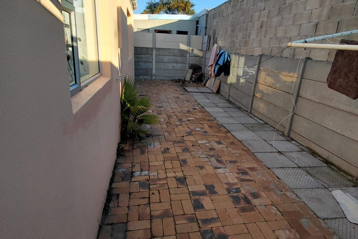 A side exterior walkway featuring brick paving, bordered by the house wall and a concrete boundary wall.