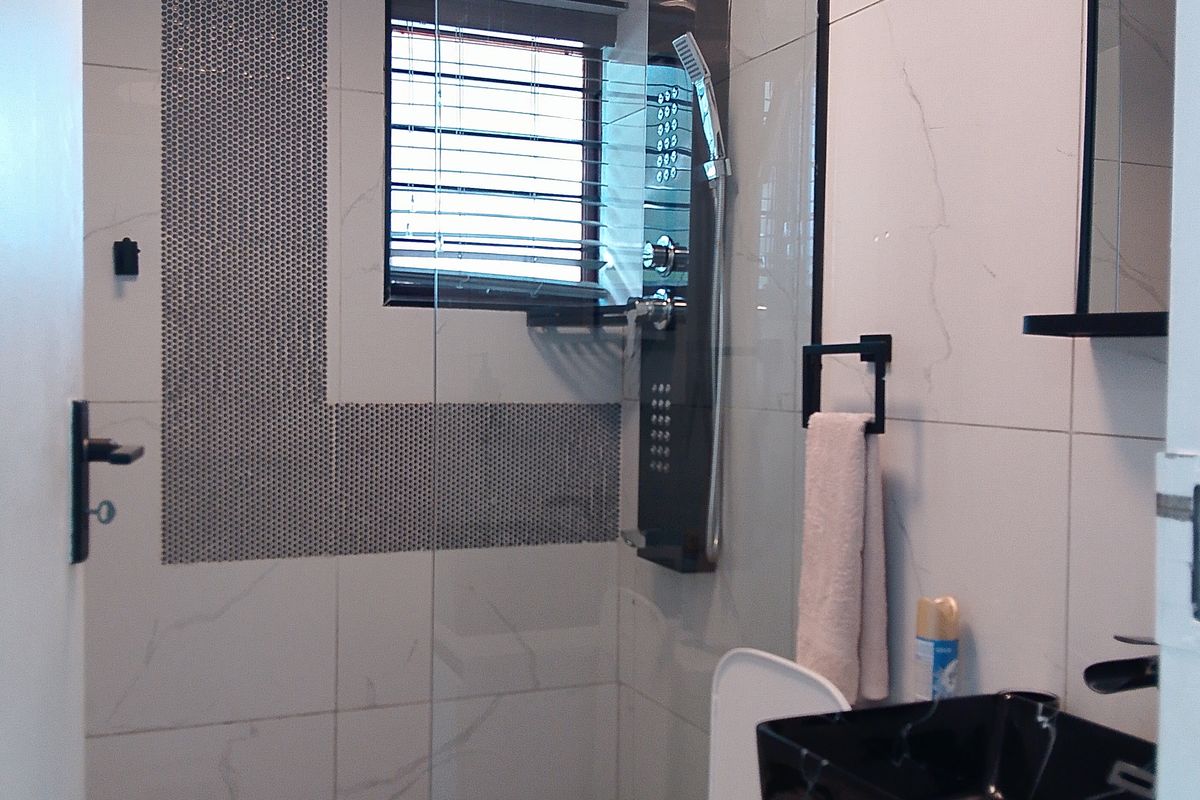 Modern bathroom featuring a glass-enclosed shower with a rainfall showerhead, geometric floor tiling, and a contemporary black vessel sink vanity.