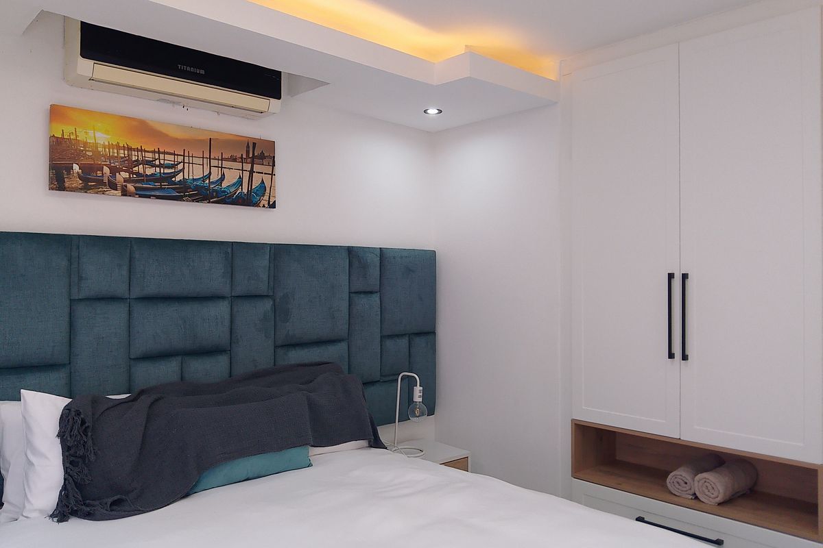 A modern bedroom featuring a built-in wardrobe with open shelving, recessed ceiling lighting, and a wall-mounted air conditioning unit.