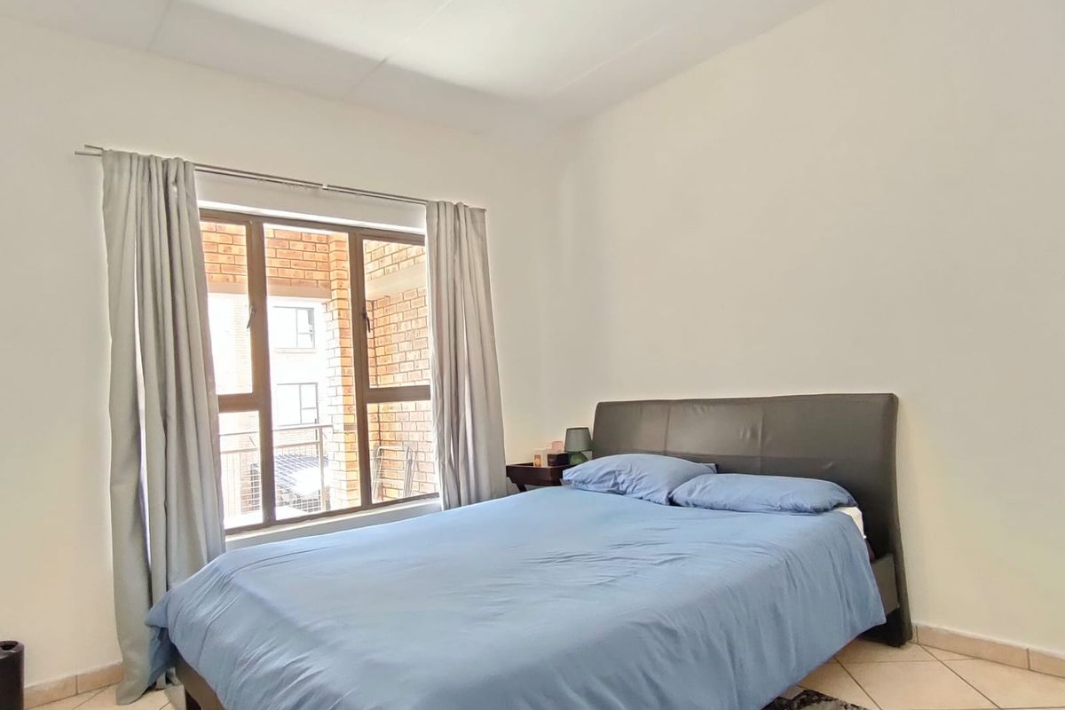 A functional bedroom featuring tiled flooring and a central ceiling light fixture, with natural light provided by a window overlooking the exterior.