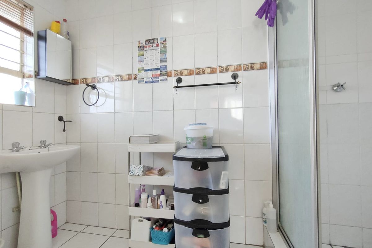 A functional bathroom featuring a pedestal basin, tiled walls and flooring, and a glass-enclosed shower unit.
