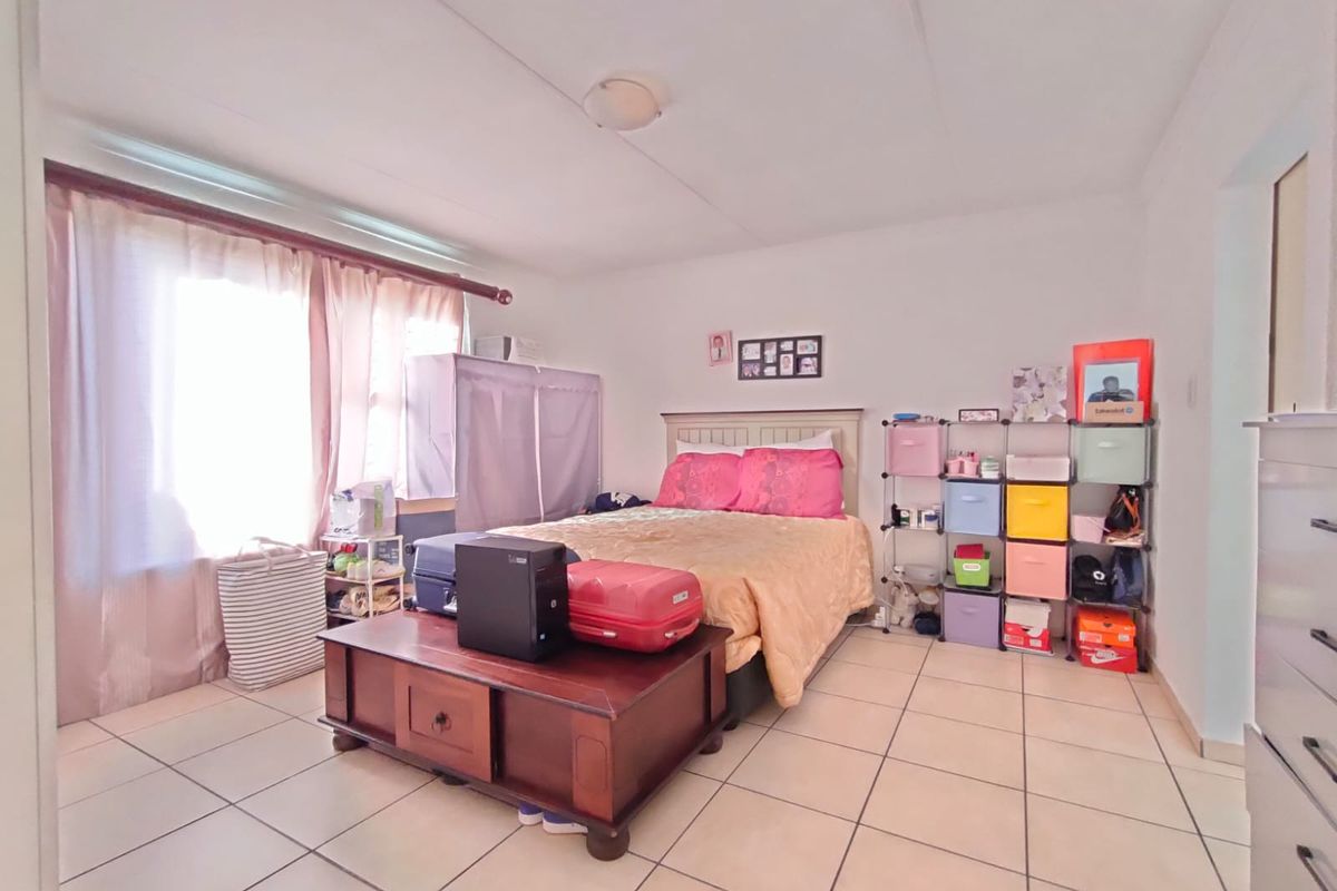 A standard bedroom featuring tiled flooring and a large window with a curtain rod, providing a functional space for rest.