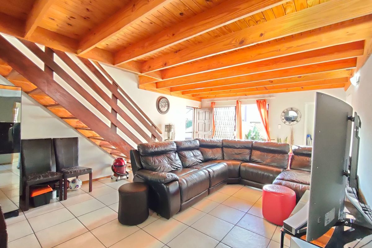 Spacious living area featuring exposed timber ceiling beams, tiled flooring, and a timber staircase leading to the upper level.