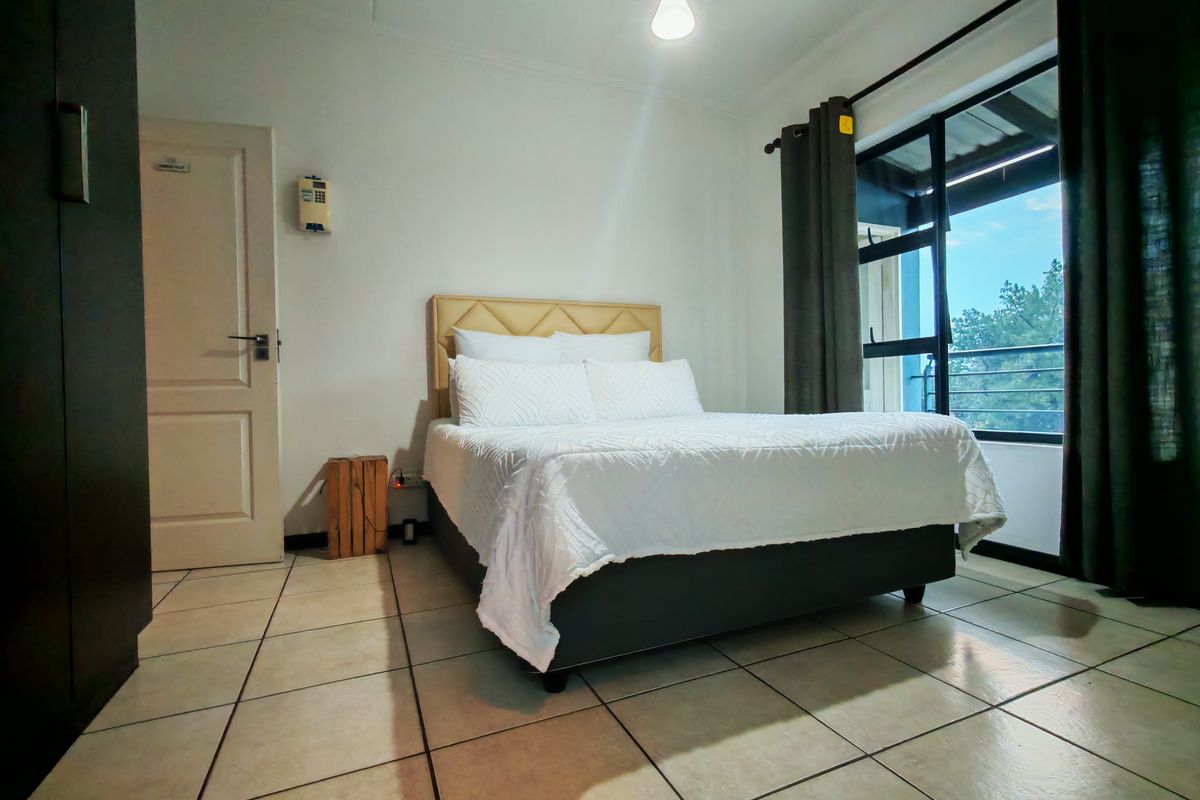 A bedroom featuring tiled flooring, a large window with natural light, and a built-in door, providing a functional and bright living space.