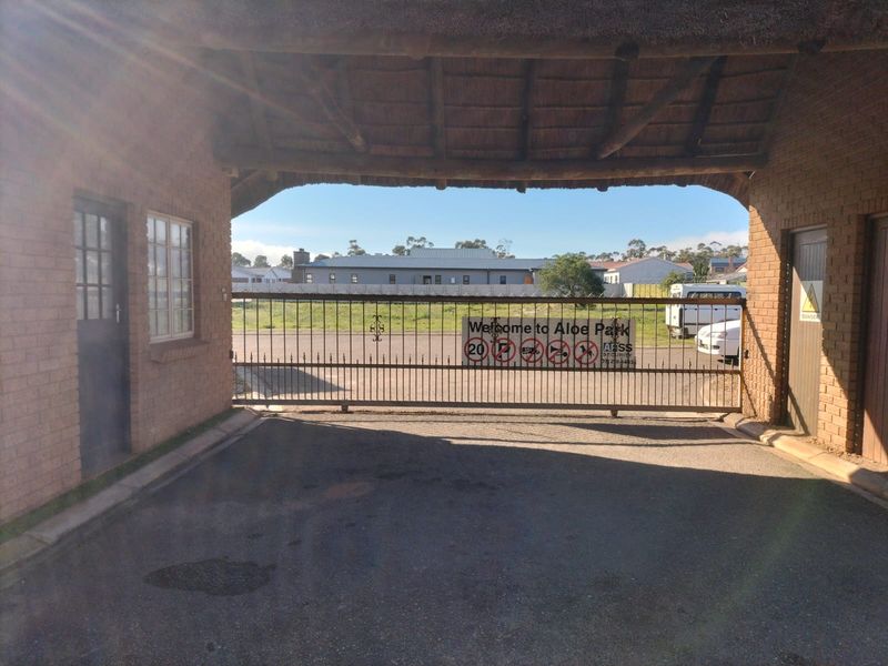 Entrance gate to Aloe Park featuring a thatched roof structure, brick masonry, and a secure metal sliding gate.