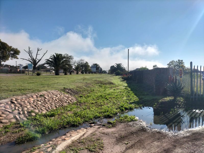 A view of the residential vacant land showing the street-facing boundary, stone-lined drainage, perimeter wall, and metal security fencing.