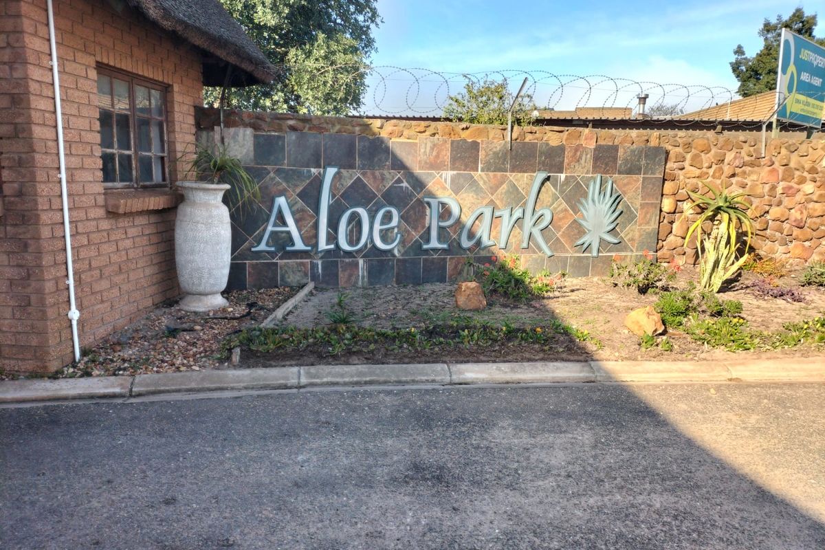 Entrance signage for Aloe Park featuring stone cladding, brickwork, and thatched roof detailing at the property boundary.
