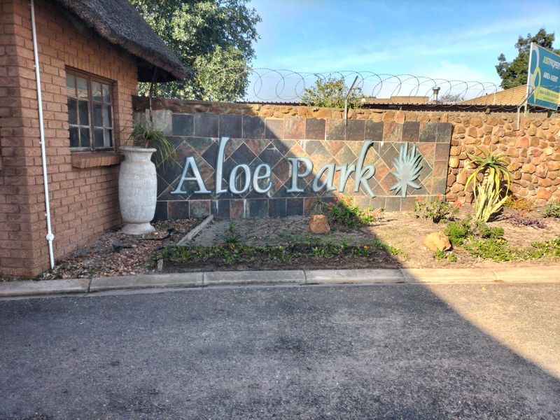 Entrance signage for Aloe Park featuring stone cladding, brickwork, and thatched roof detailing at the property boundary.