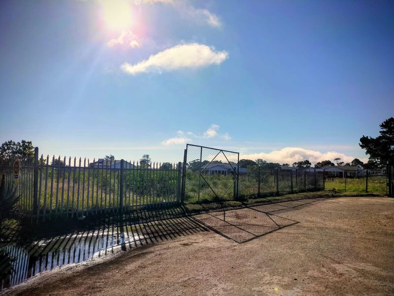 A view of a vacant residential plot featuring metal perimeter fencing and a gate, accessible via an unpaved road.