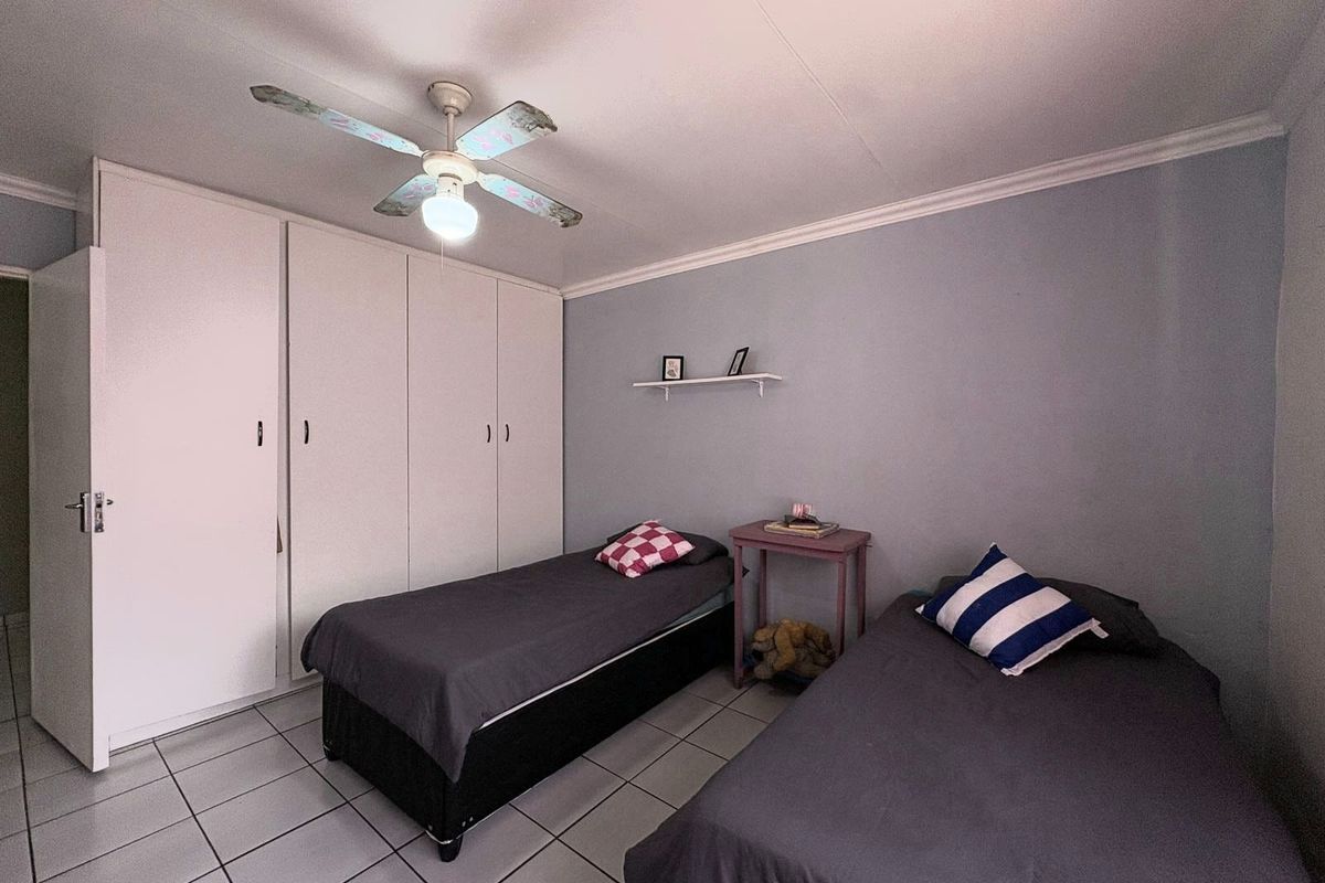 A bedroom featuring tiled flooring, built-in cupboards, and a ceiling fan, providing a functional space with neutral wall finishes.