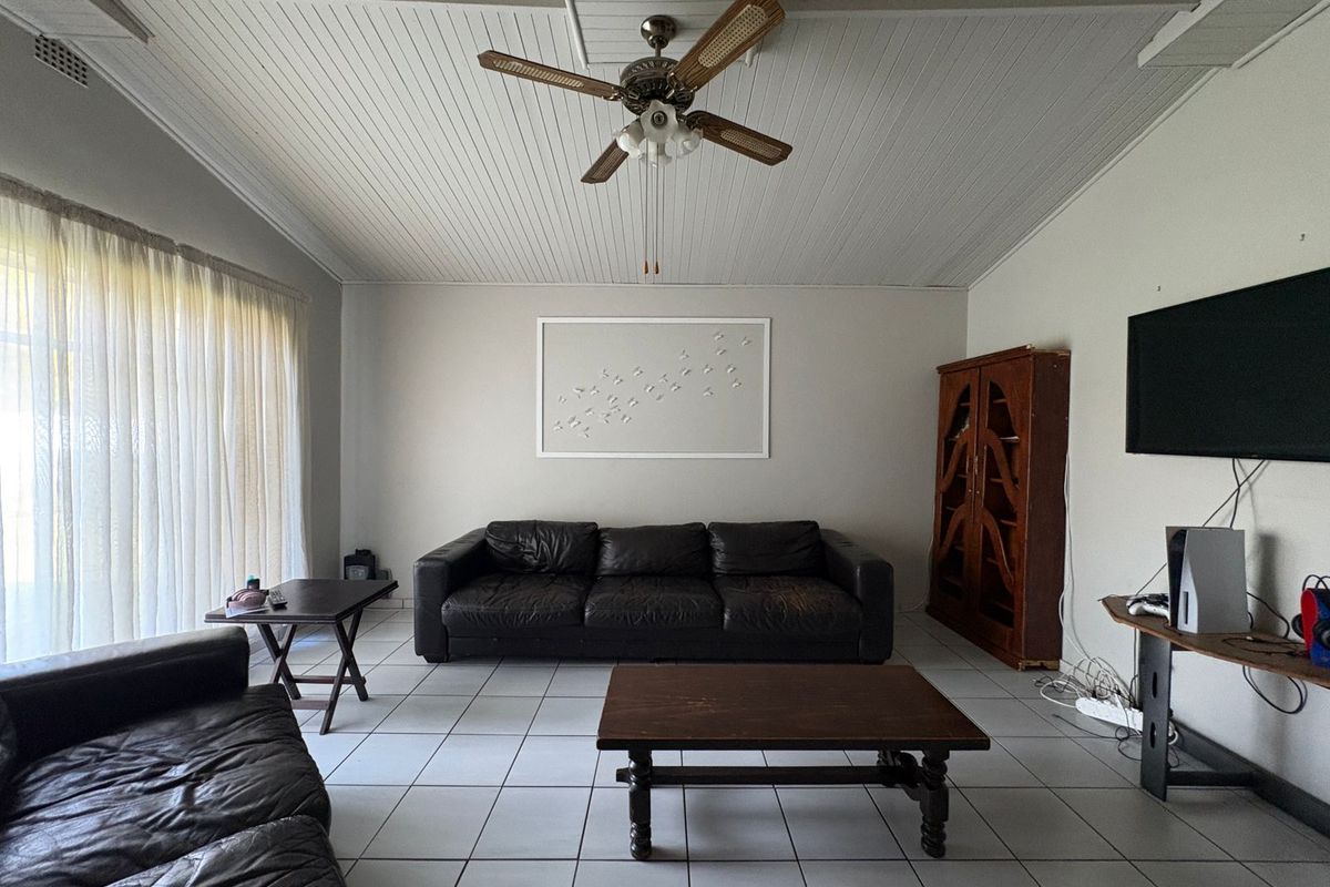A spacious living room featuring tiled flooring, a tongue and groove ceiling, and a central ceiling fan.
