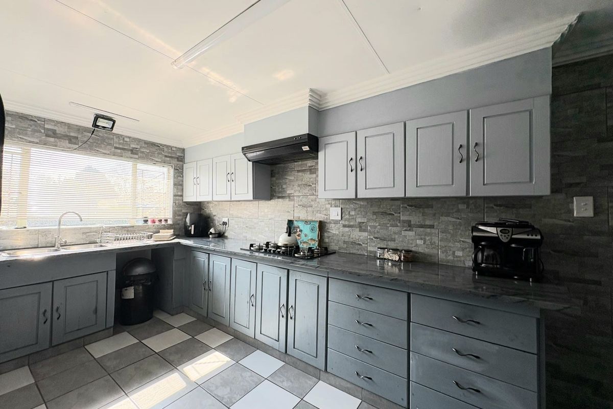 A functional kitchen featuring grey cabinetry, stone-look tiled backsplash, gas hob with extractor, and tiled flooring with ample counter space.