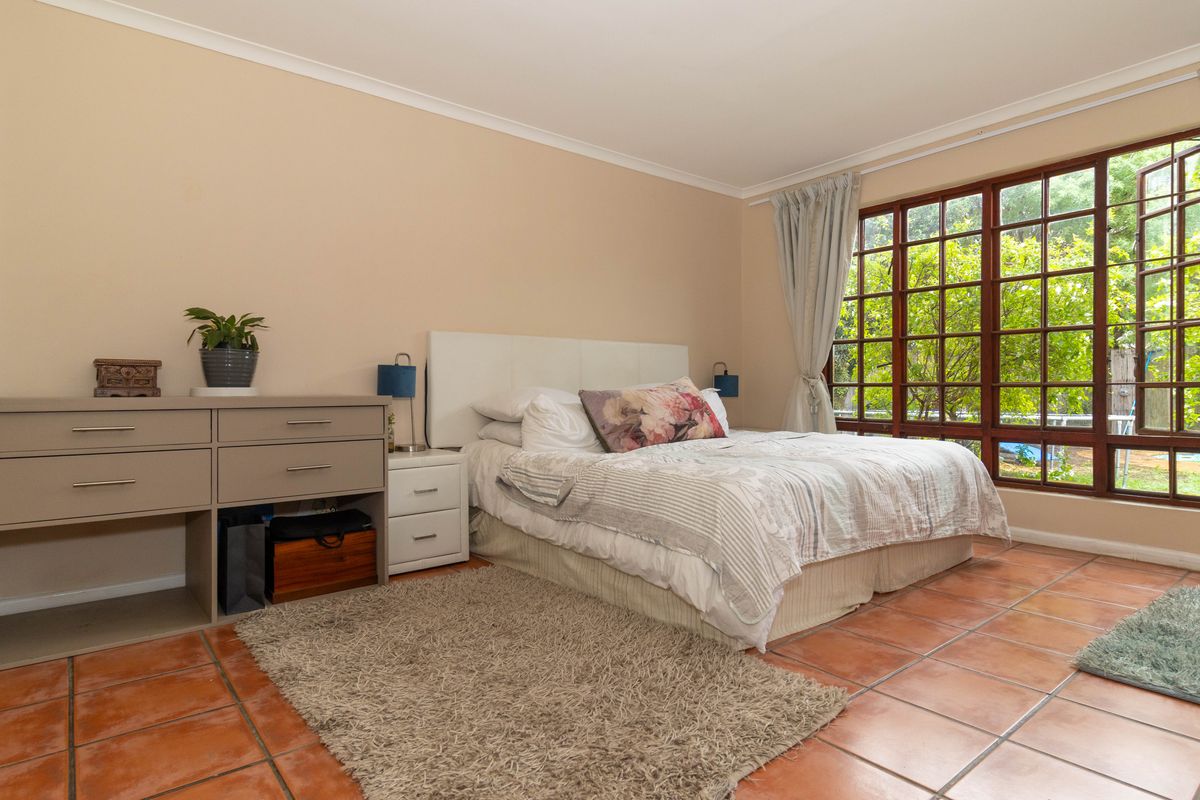 A spacious bedroom featuring terracotta floor tiles, large timber-framed windows with garden views, and neutral wall finishes.