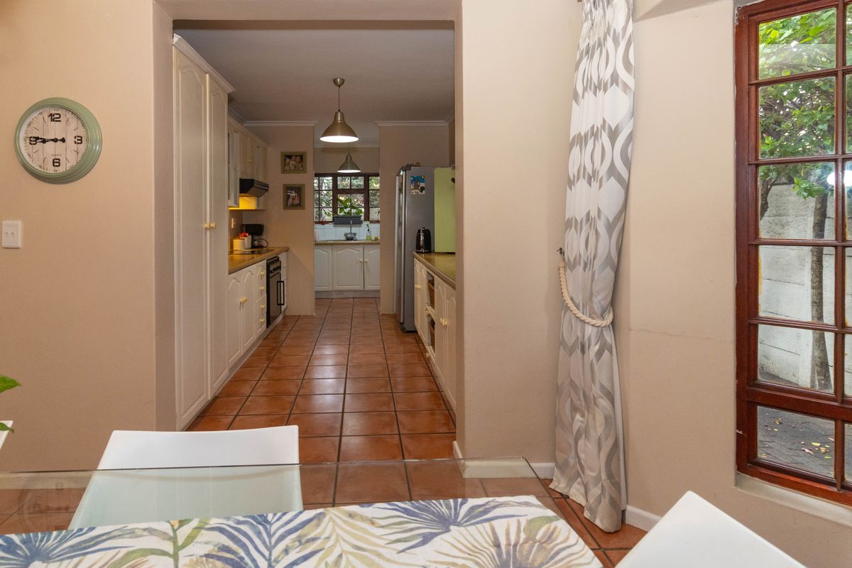 A functional kitchen featuring tiled flooring, built-in cabinetry, and a secondary prep area, with direct access to the garden through a wooden framed window.