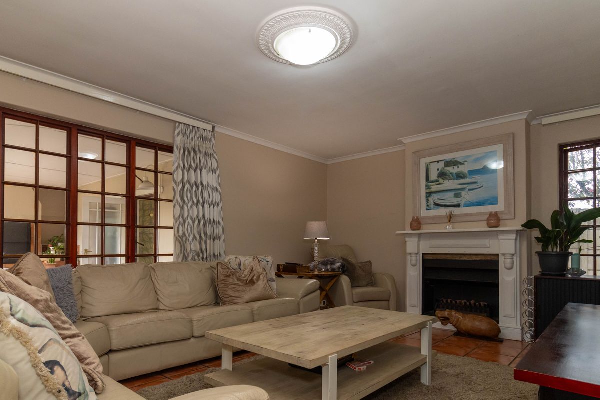 A comfortable living room featuring a classic fireplace, decorative ceiling rose, and large wooden-framed windows providing natural light.