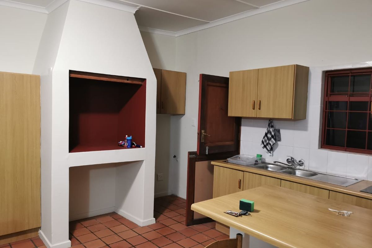 Kitchen area featuring a built-in indoor braai fireplace, wooden cabinetry, double basin sink, and terracotta floor tiles.