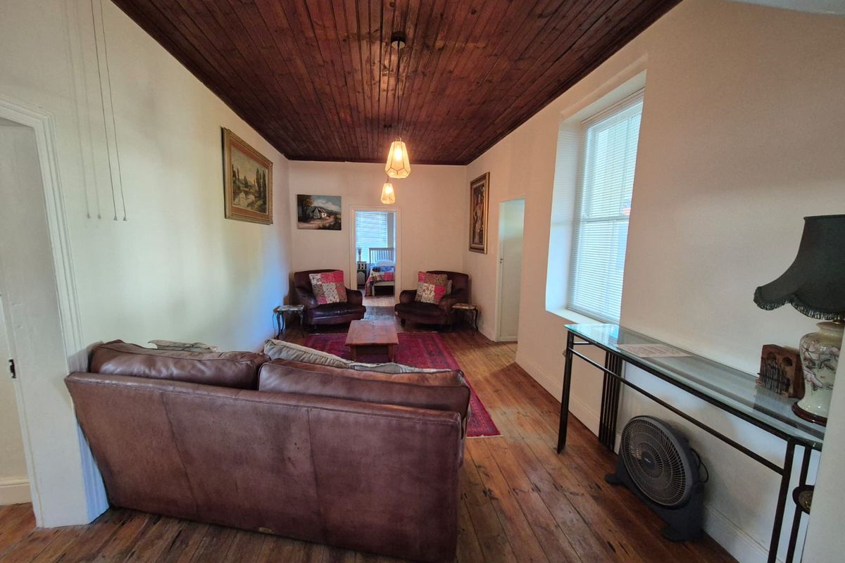 A living room featuring a distinctive dark timber-paneled ceiling, polished wooden floors, and natural light through a side window.